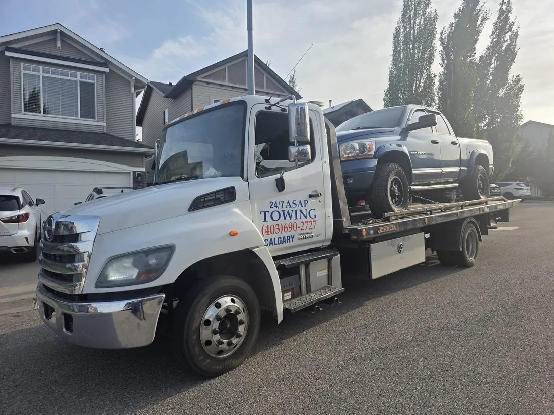 24/7 ASAP Towing flatbed truck loaded with a pickup truck in a Calgary driveway