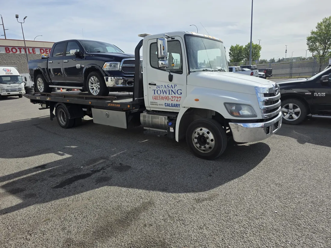24/7 ASAP Towing flatbed truck with a pickup truck loaded, parked in a Calgary commercial lot