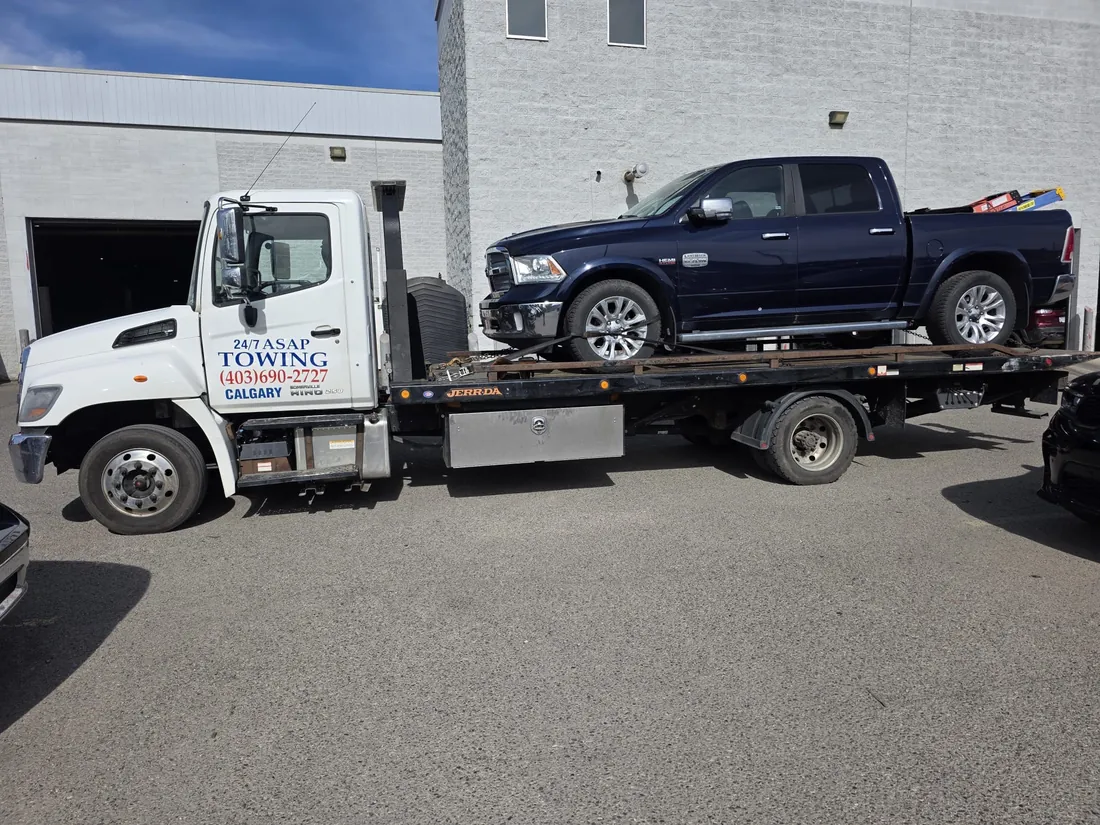 24/7 ASAP Towing flatbed truck loaded with a pickup truck at a Calgary industrial yard