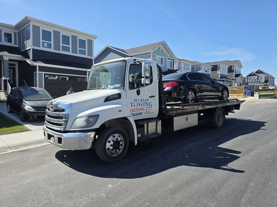 24/7 ASAP Towing flatbed carrying a sedan in a Calgary neighbourhood