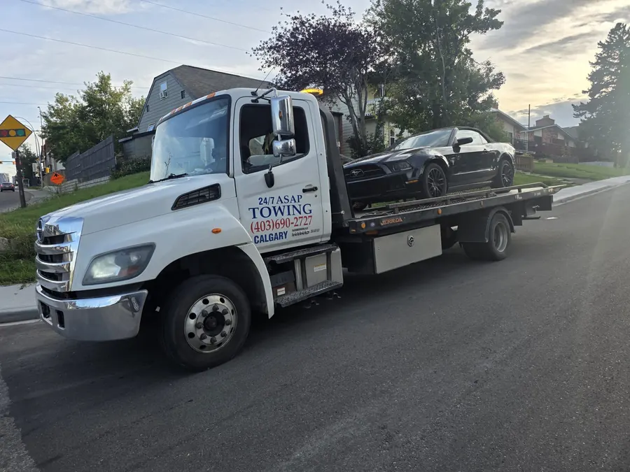 24/7 ASAP Towing flatbed transporting a convertible on a Calgary street at dusk